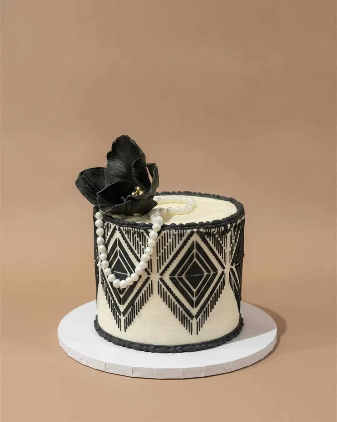 Ivory cake with black art deco piped geometry, draped pearls and a black sugar flower