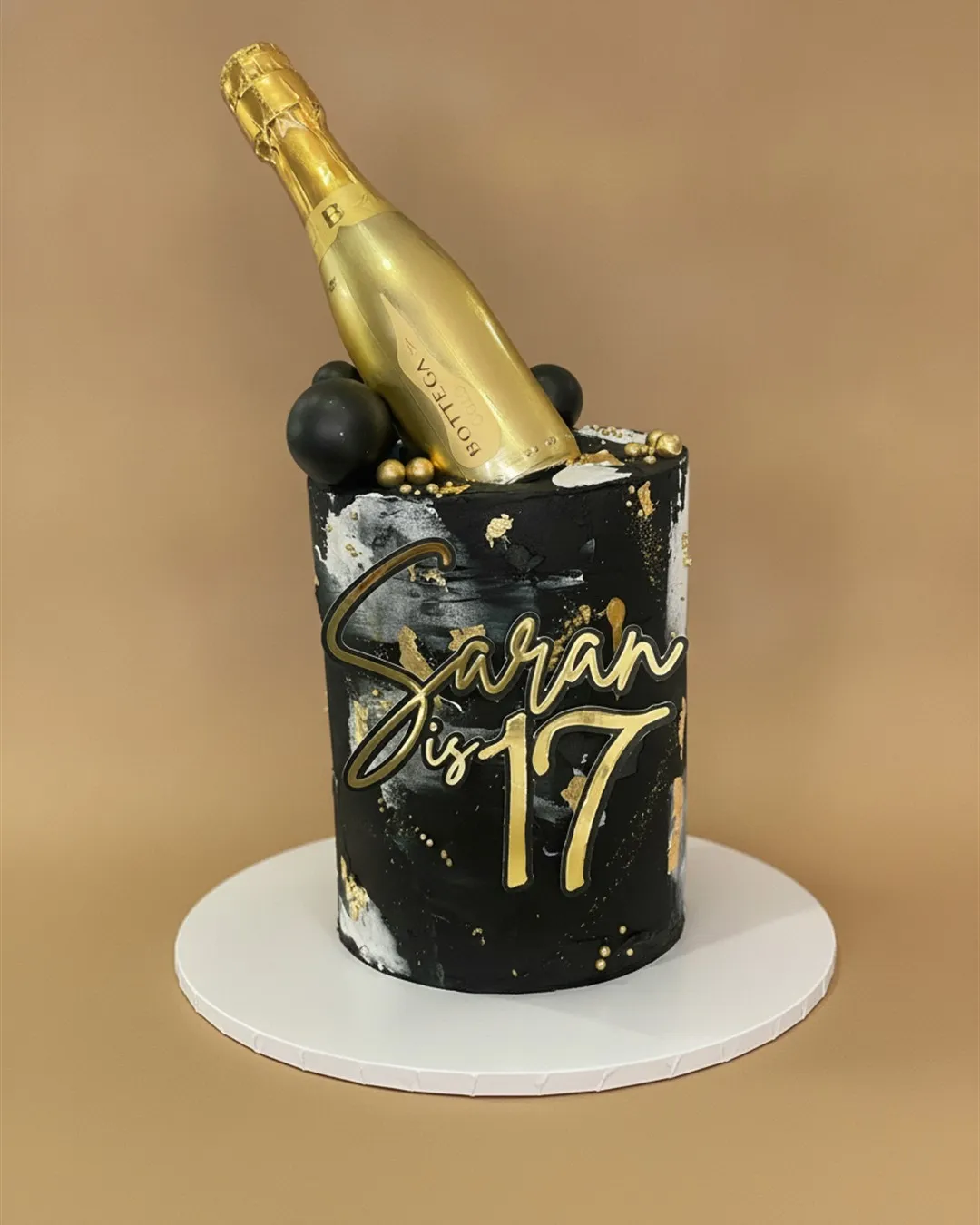 Black and gold cake with a sugar bottle topper and metallic gold detailing