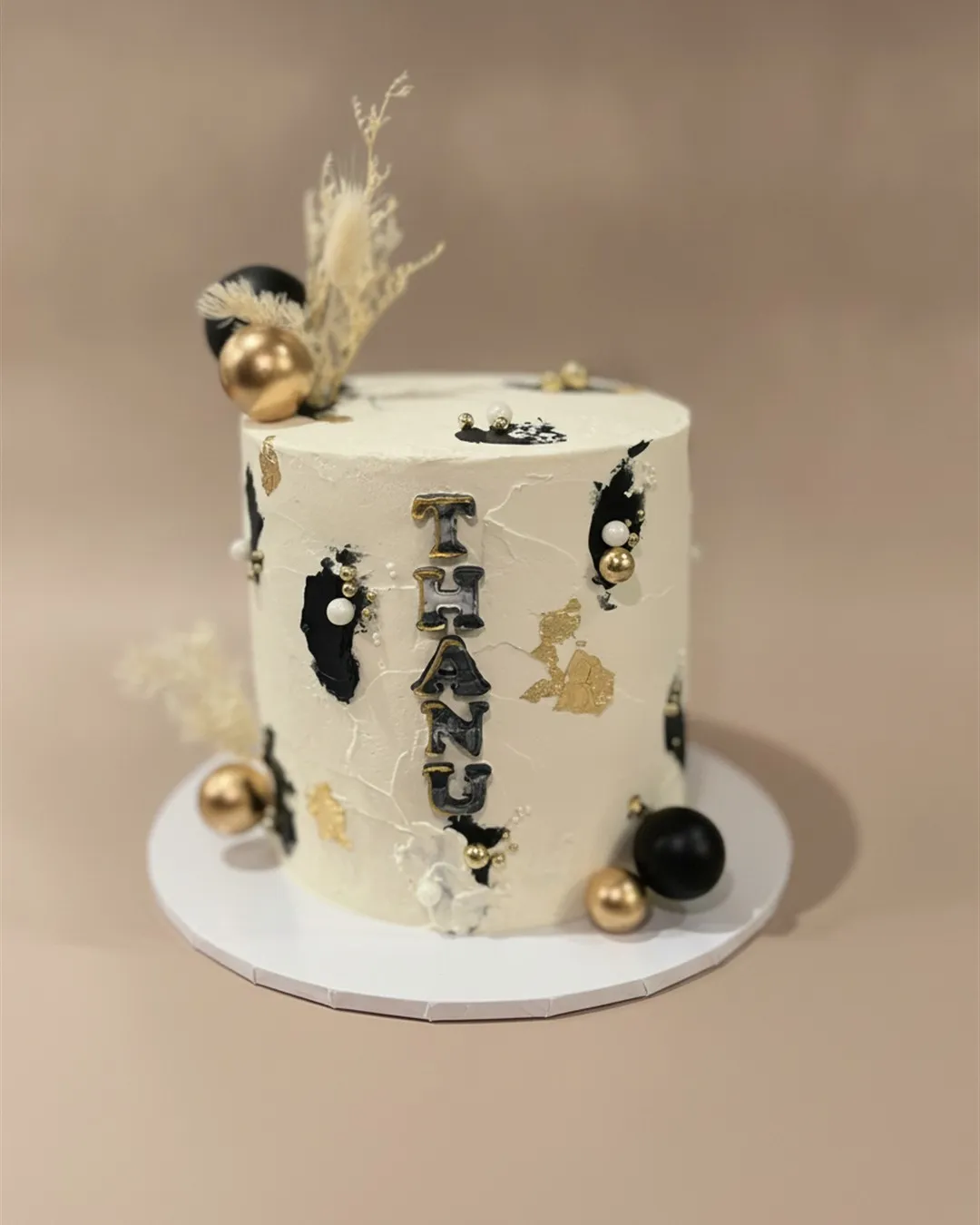 Cream cake with black and gold abstract detailing, gold baubles and dried floral accents