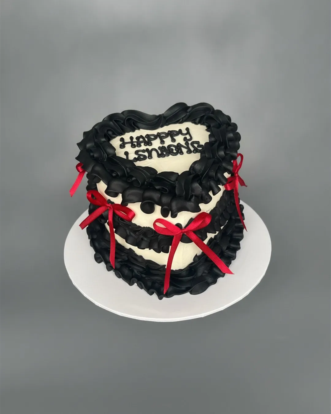Black ruffled heart-shaped cake finished with red satin bows, photographed from above