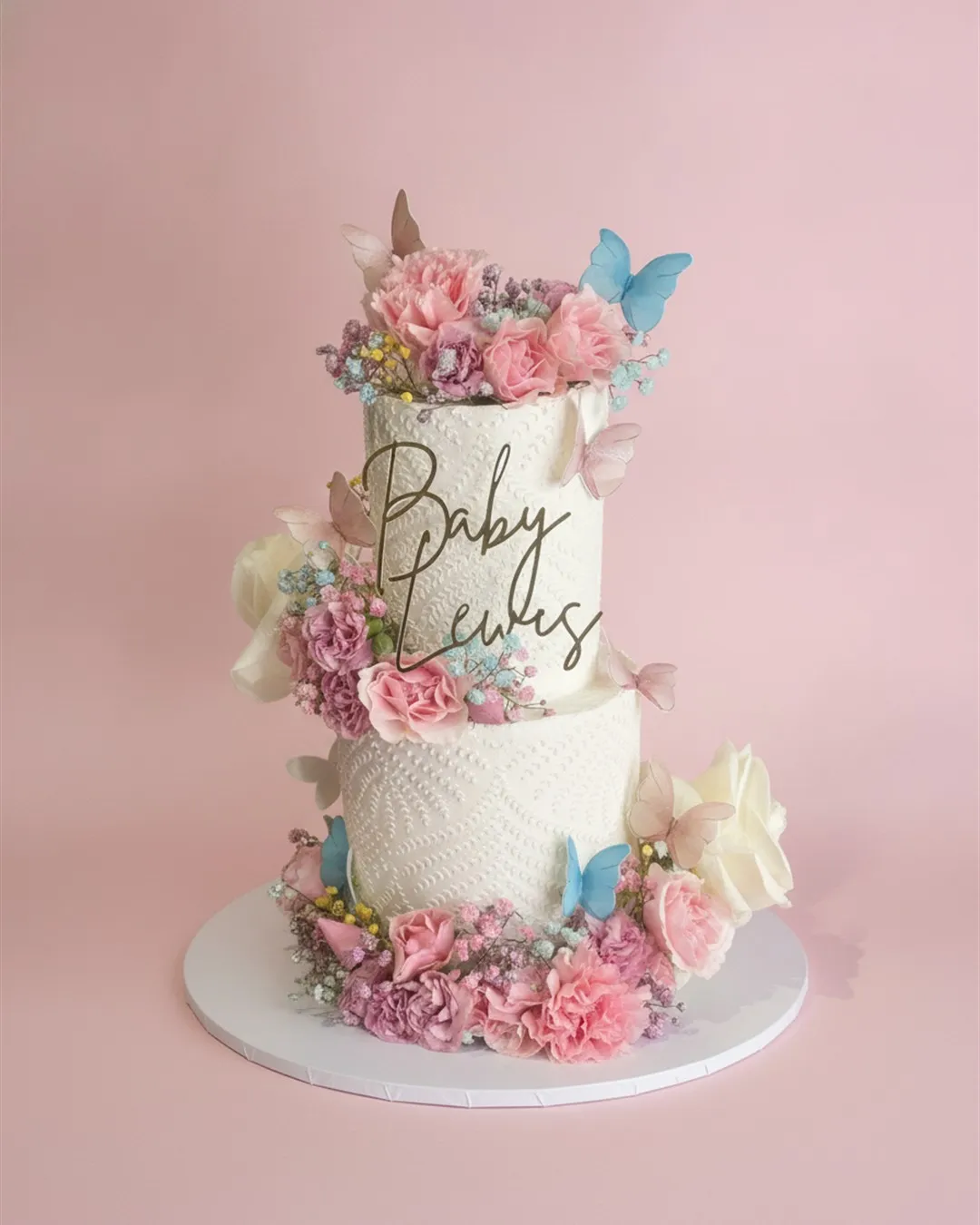 Two-tier textured white cake surrounded by blush fresh flowers and pastel sugar butterflies