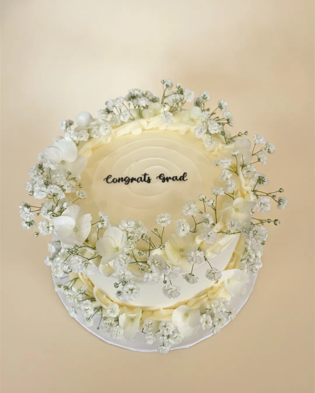 Ivory graduation cake topped with baby's breath and white hydrangea reading Congrats Grad
