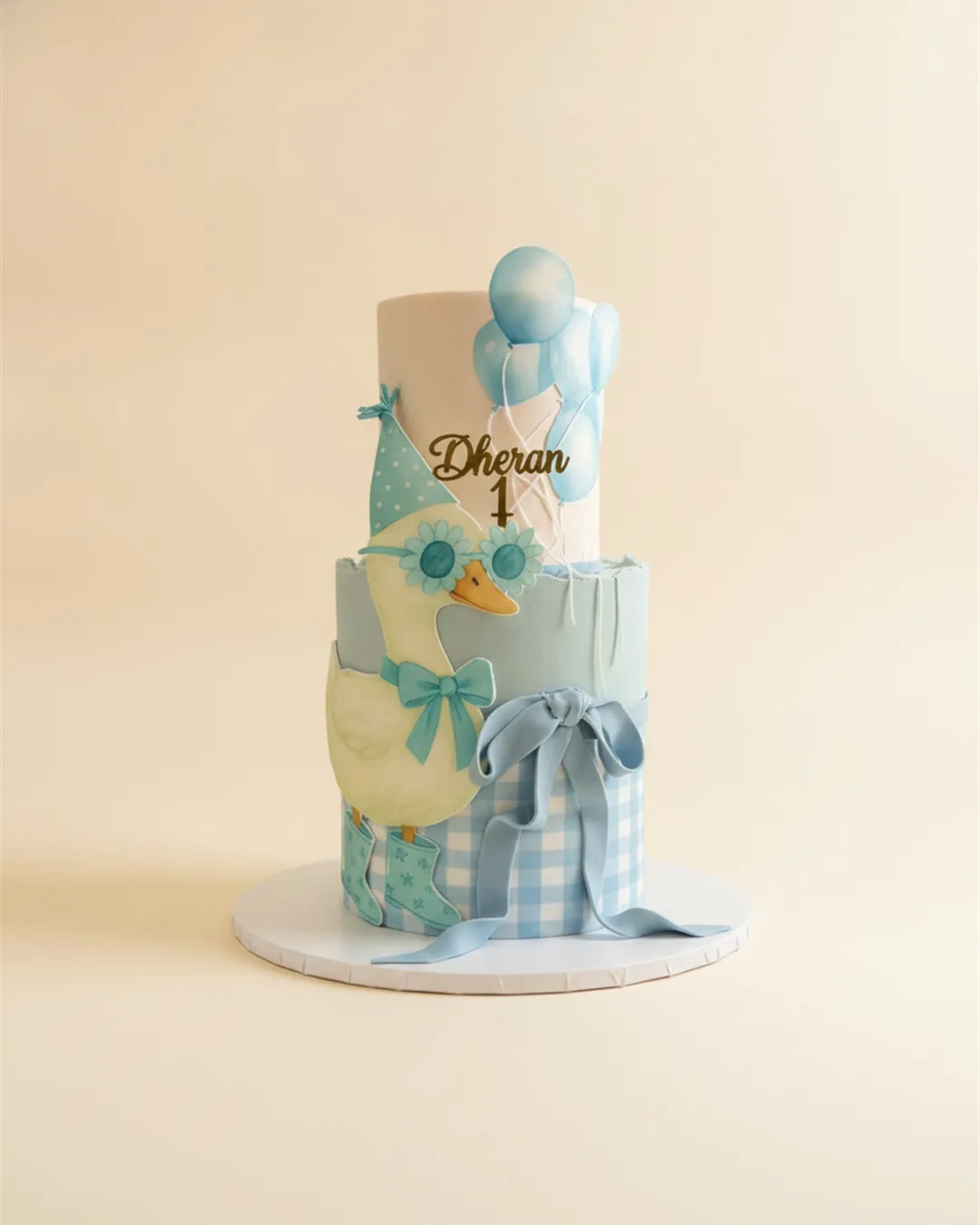 Two-tier blue gingham cake with a sugar duckling and pastel balloon decorations