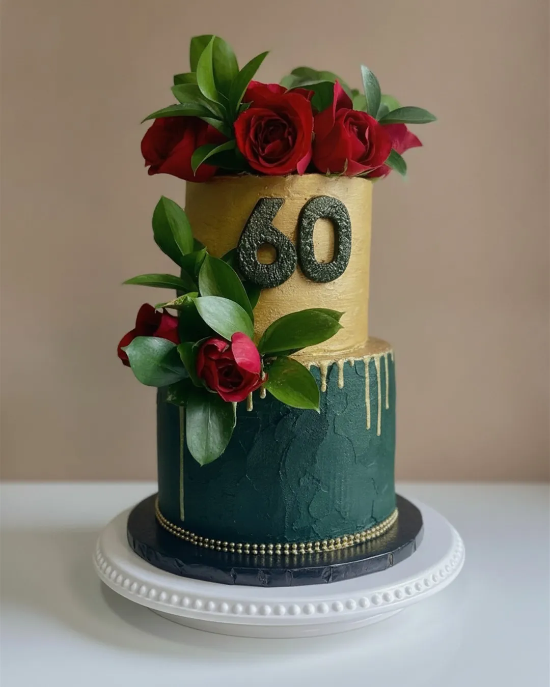 Two-tier gold and deep green cake with fresh red roses and a milestone number topper