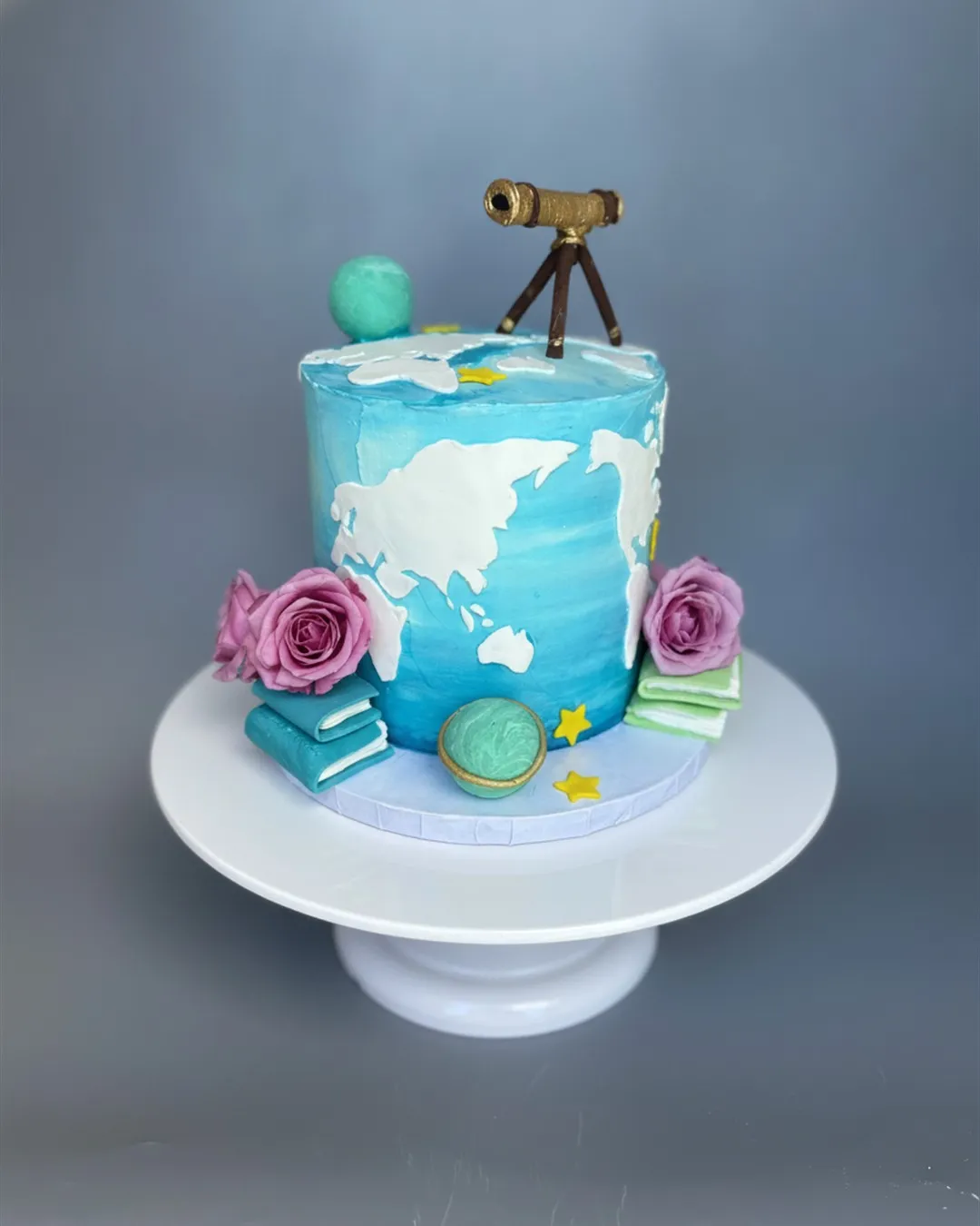 Hand-painted world globe birthday cake with a gold telescope topper, purple roses and stacked books