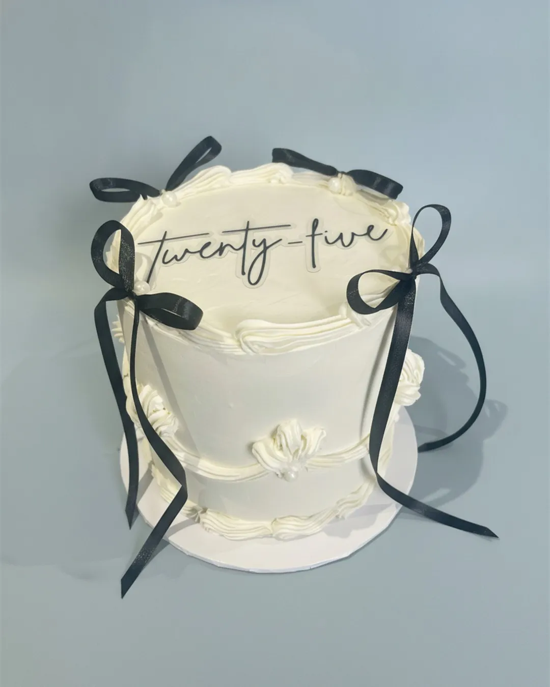 Ivory buttercream cake dressed with black satin bows and a script twenty-five topper