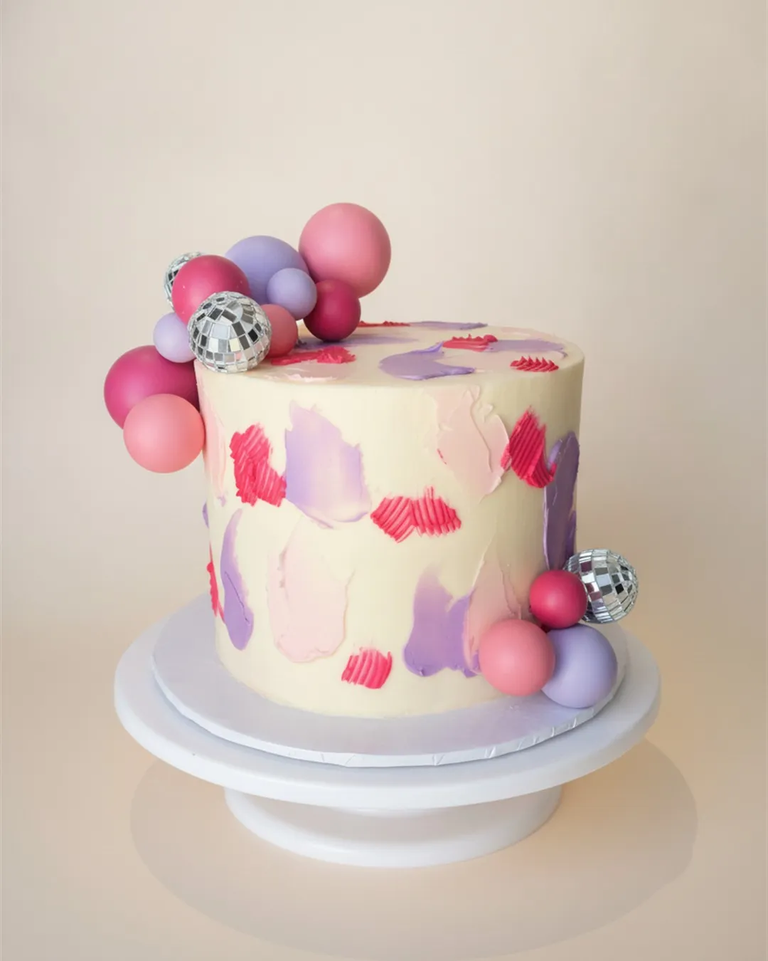 Cream cake with pink and purple palette-knife strokes, sugar spheres and disco ball accents