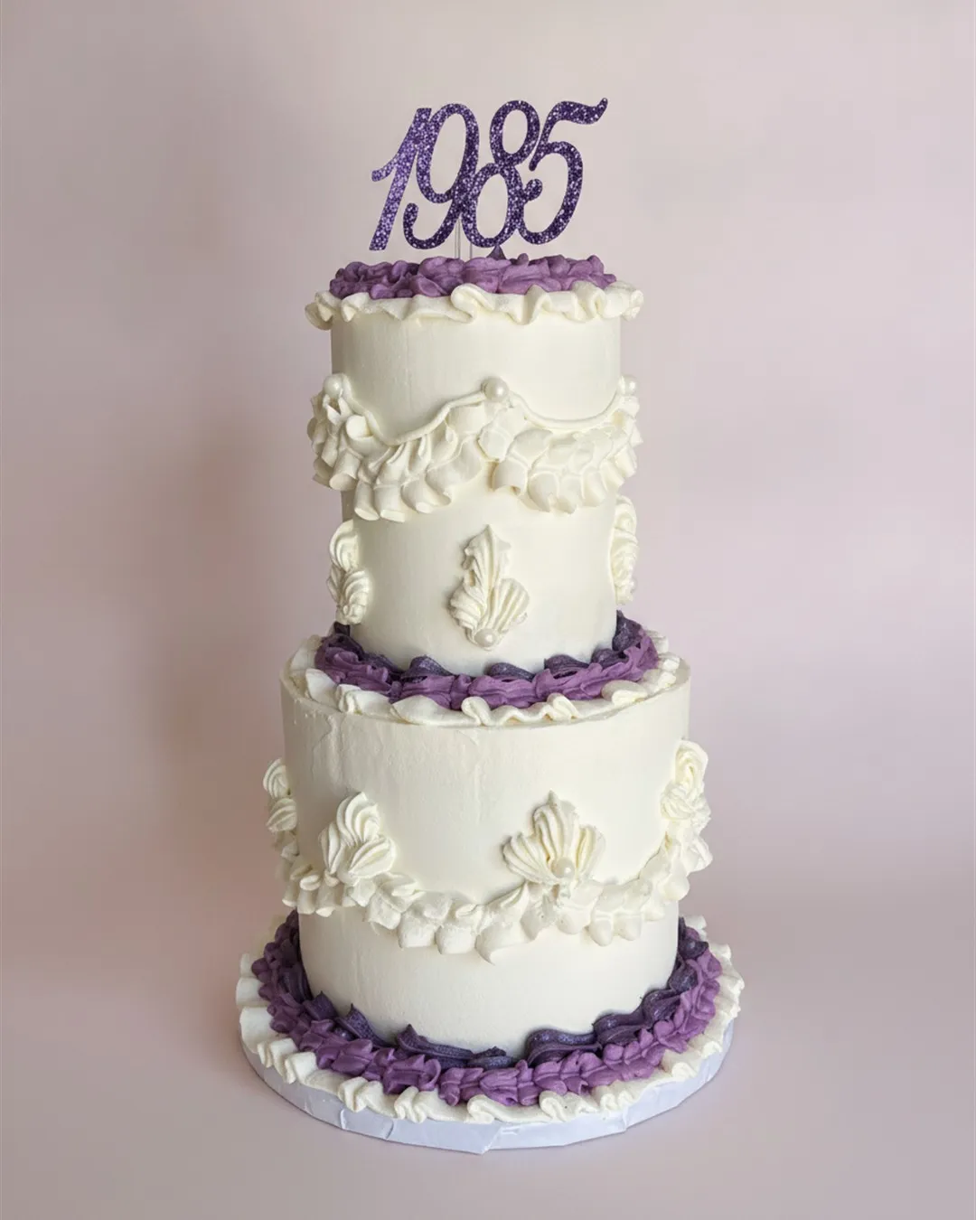 Two-tier white and purple vintage Lambeth cake with piped scrollwork and a glitter year topper