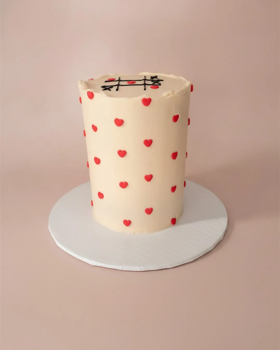 Cream buttercream cake covered in small piped red hearts with a fine wire topper