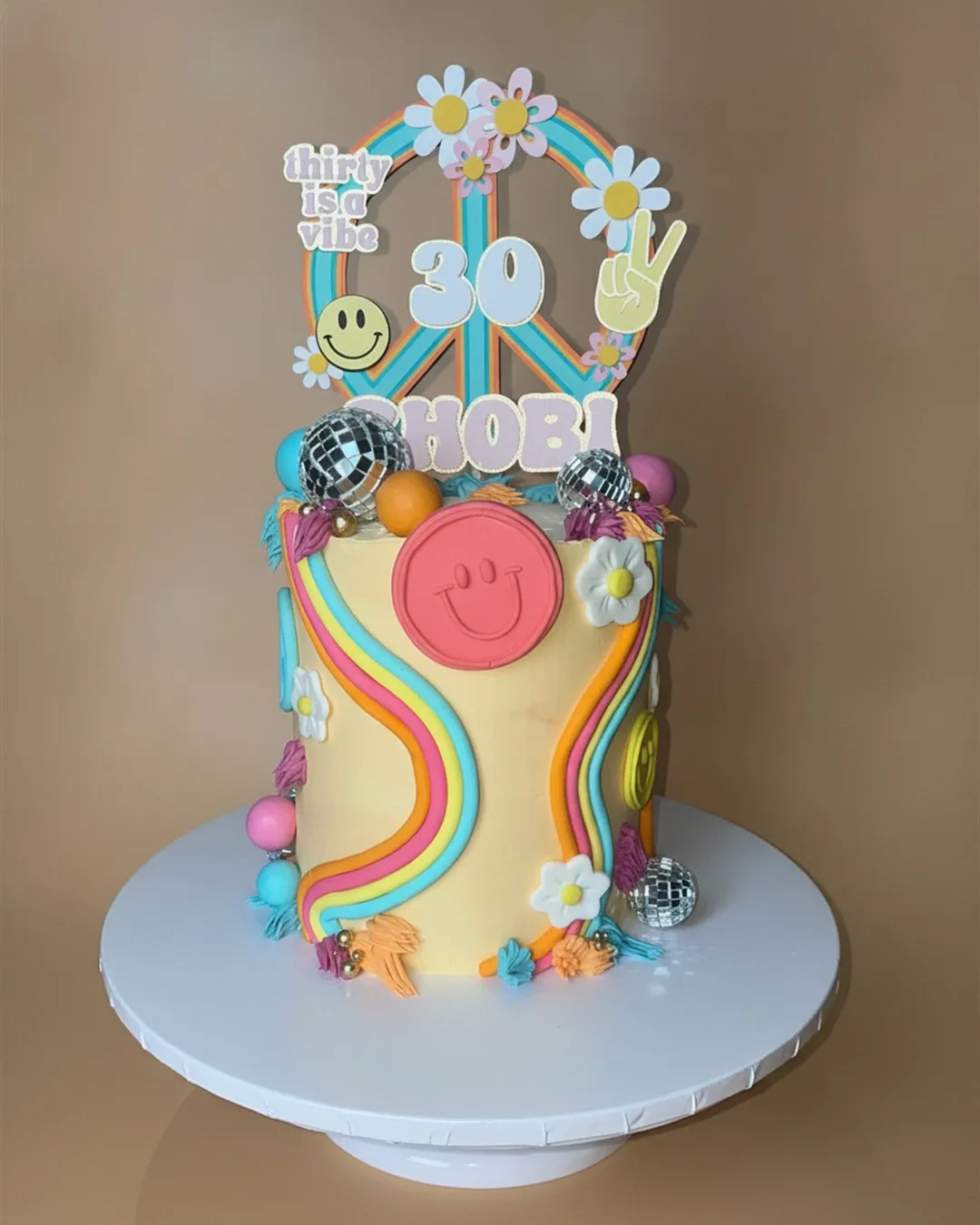 Bright retro cake with rainbow swirls, daisies, smiley face and disco ball decorations