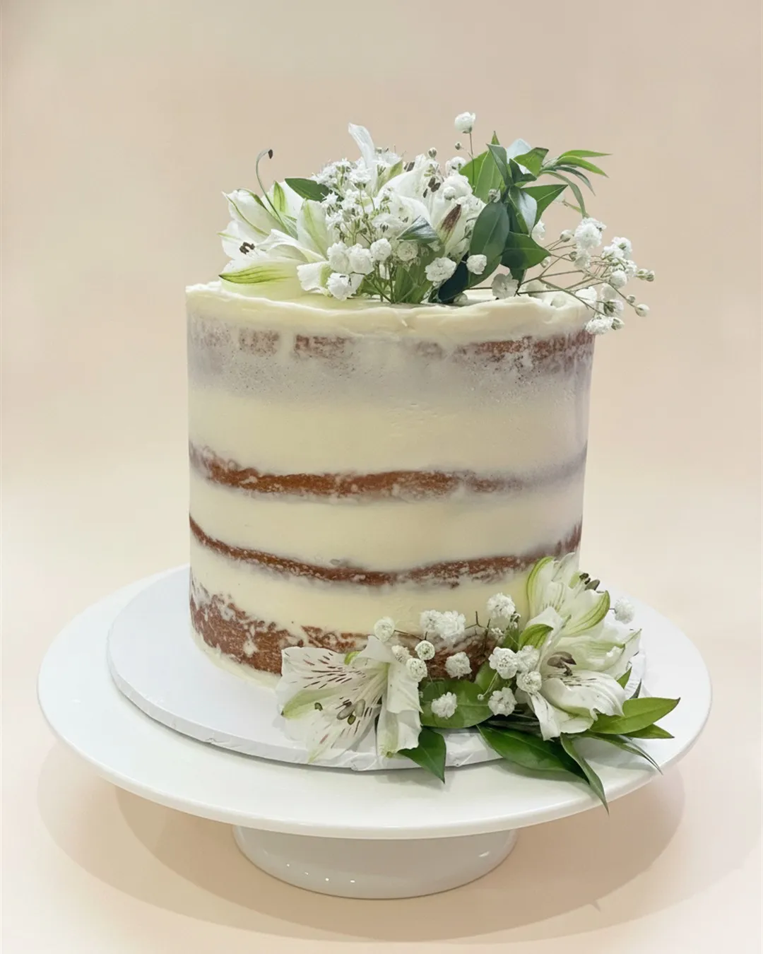 Semi-naked buttercream cake topped and based with white lilies and fresh greenery
