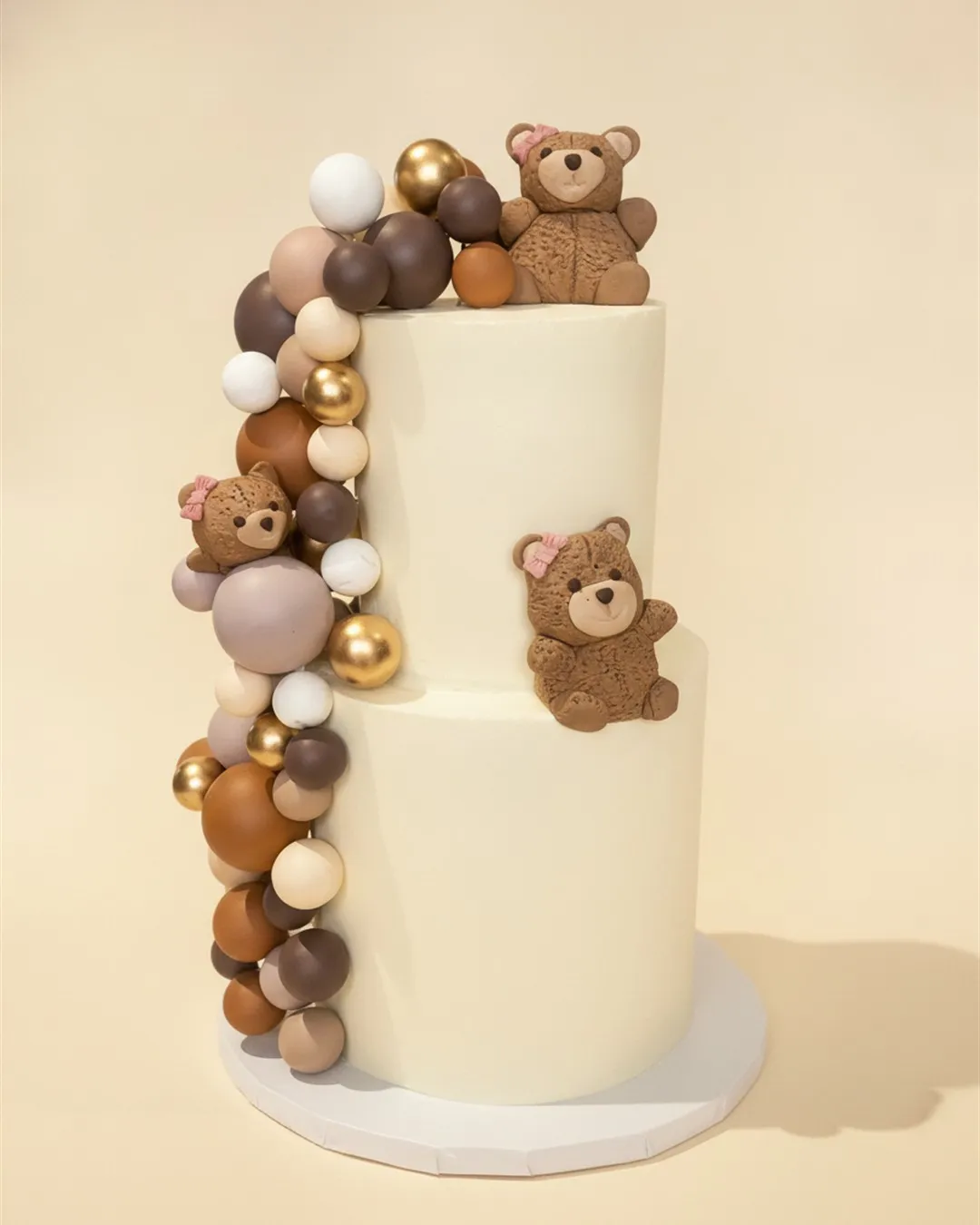 Two-tier offset ivory cake with sugar teddy bears and a brown and gold sugar balloon garland