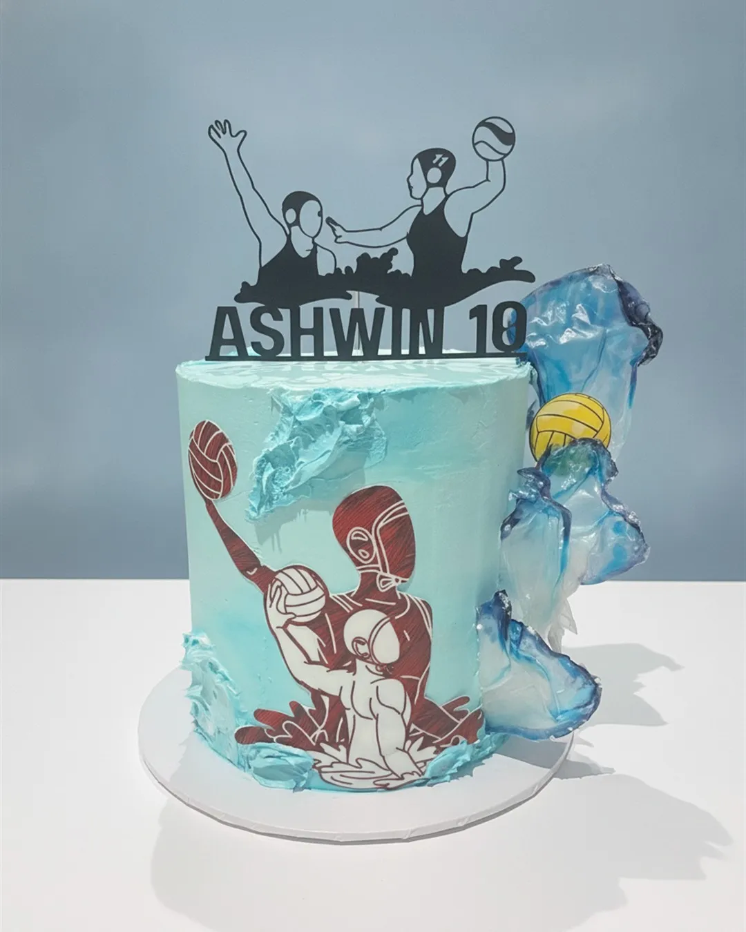 Blue and red water polo themed cake with edible printed players and a sugar ball topper
